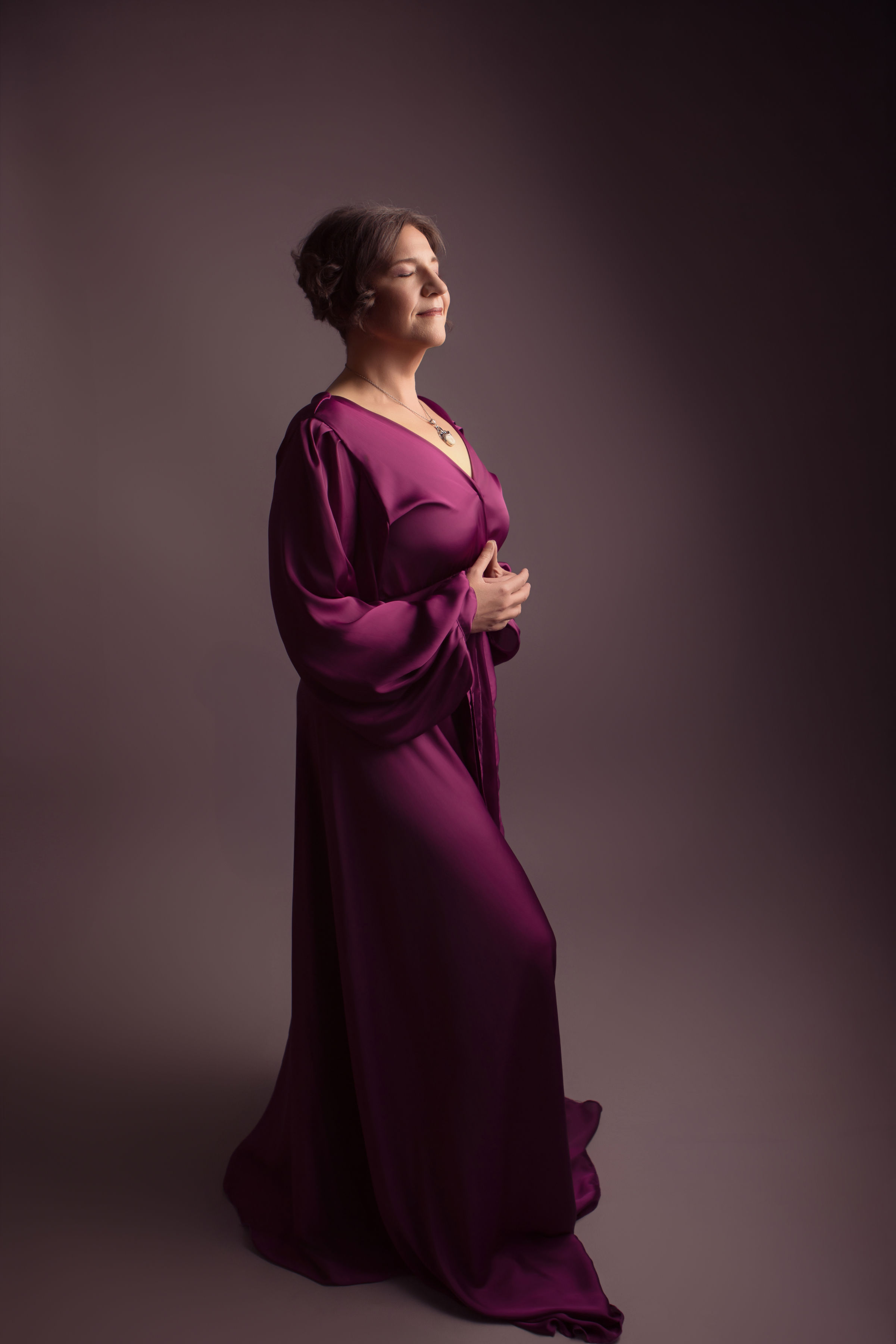 Mandy Kuelz in a plum silk gown, eyes closed and hands resting over her heart
